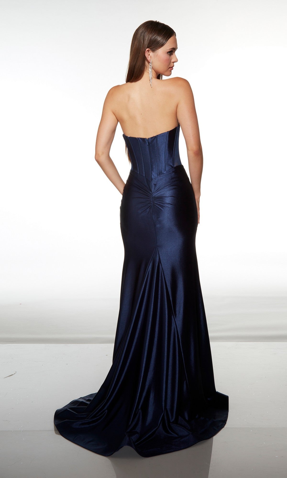 A woman in the Alyce 62156 stands facing away, showcasing the dark blue satin gown’s structured bodice, floor-length skirt, and elegant beaded sweetheart neckline.